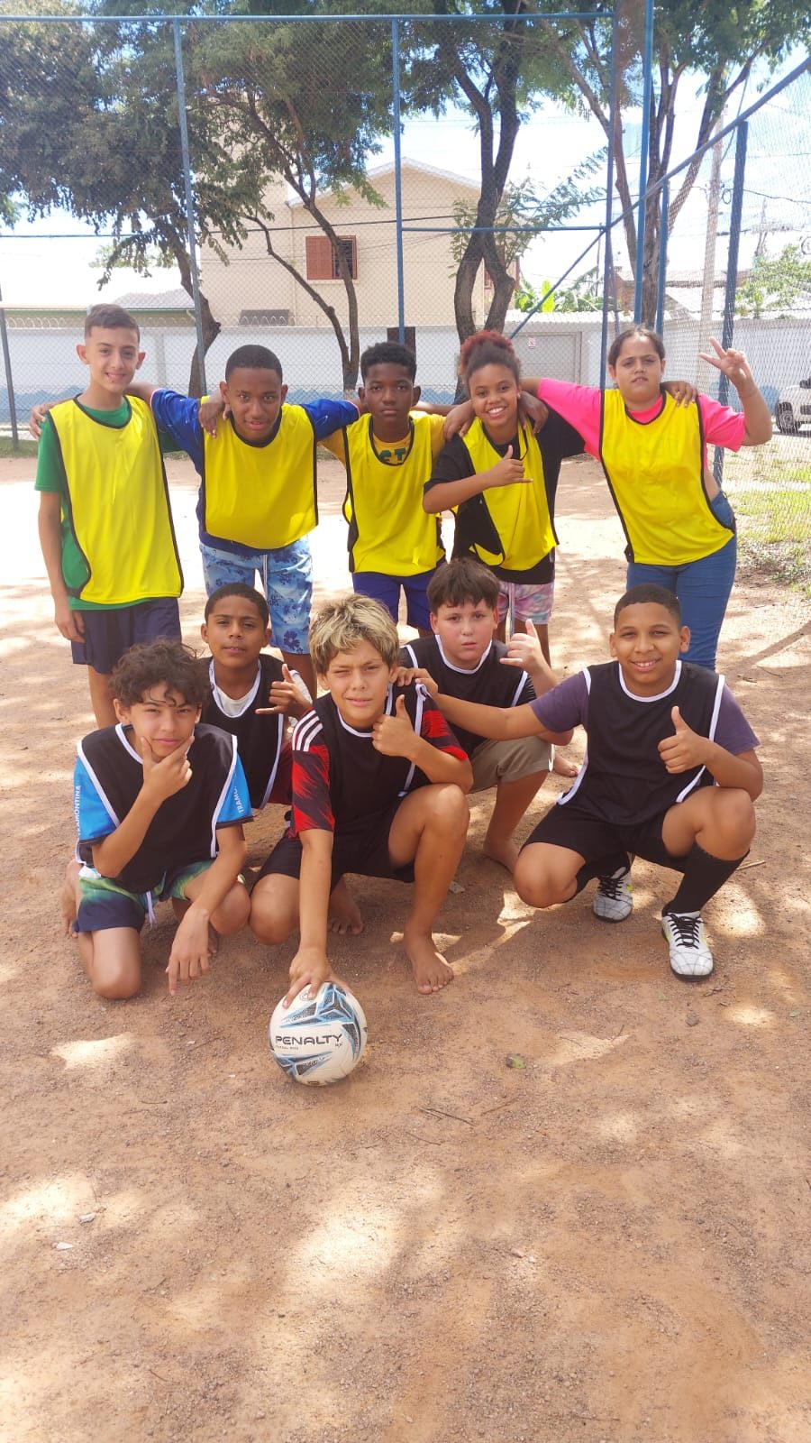 Meninos de colete posando com bola após jogo na praça