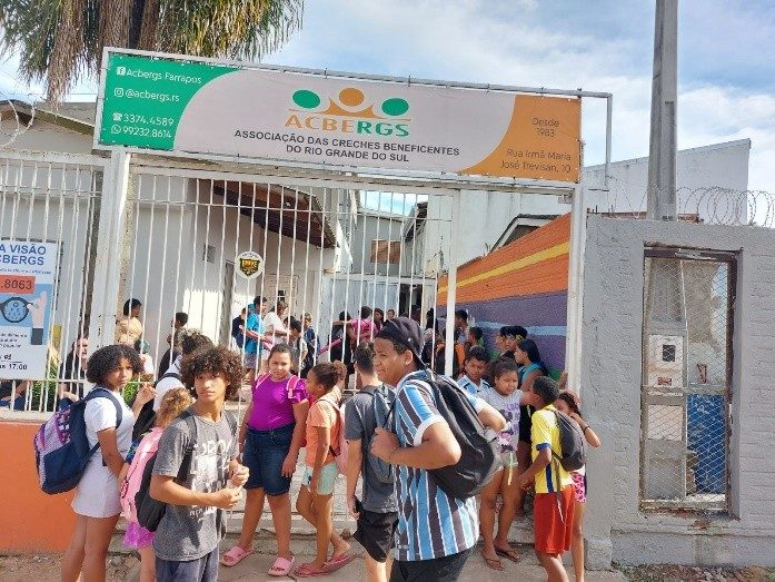 Adolescentes chegando ao portão da ACBERGS, sob a placa da instituição
