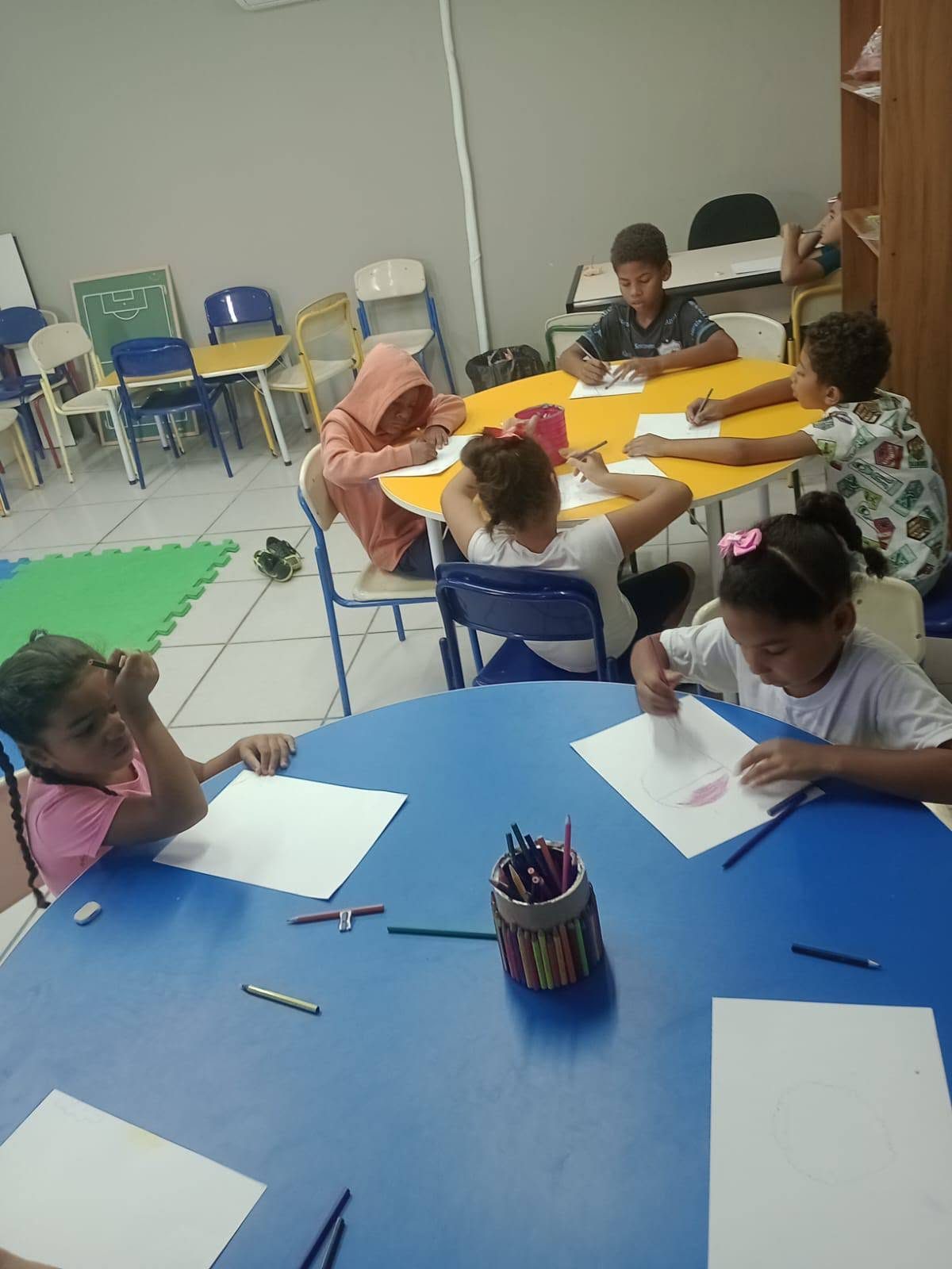 Crianças desenhando em mesas na sala de atividades da ACBERGS